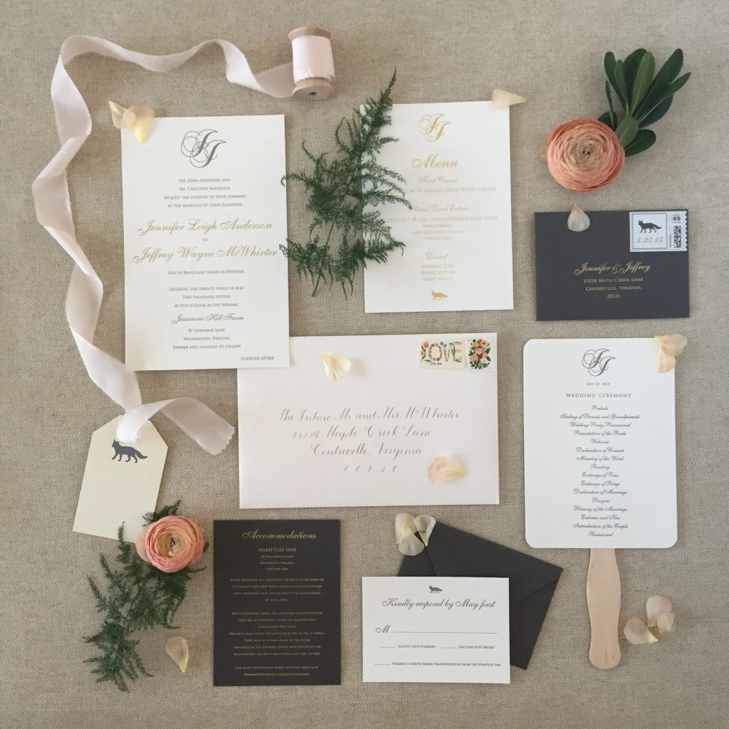Elegant wedding invitation suite flat lay featuring ceremony and menu cards, RSVP, envelope with calligraphy, and silk ribbon accented with greenery and pink ranunculus flowers
