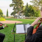 Formally dressed string duo playing violin and cello at outdoor garden wedding ceremony