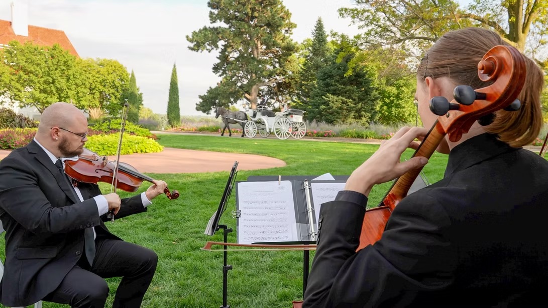 Formally dressed string duo playing violin and cello at outdoor garden wedding ceremony