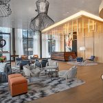 Contemporary hotel lobby featuring wood-paneled reception desk, lounge seating, and dramatic wire-frame chandeliers