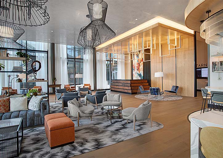 Contemporary hotel lobby featuring wood-paneled reception desk, lounge seating, and dramatic wire-frame chandeliers