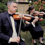Two formally dressed violinists performing outdoors in an autumn garden setting