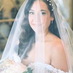 Bride wearing pearl-adorned veil with natural makeup and loose waves holding bouquet