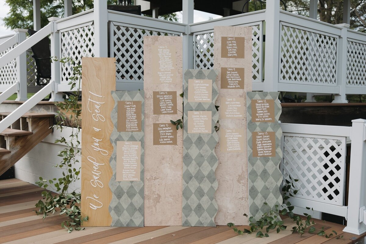 Geometric patterned seating chart display with "Find Your Seat" sign decorated with greenery garland