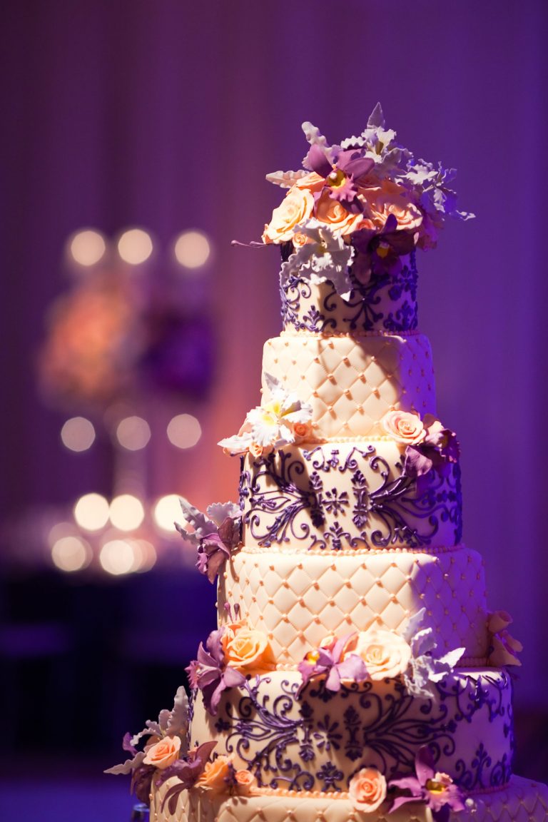Five-tier wedding cake with quilted fondant, purple scrollwork piping, and cascading peach and purple flowers