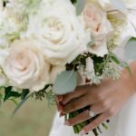 Bride holding white rose bouquet displaying diamond engagement ring