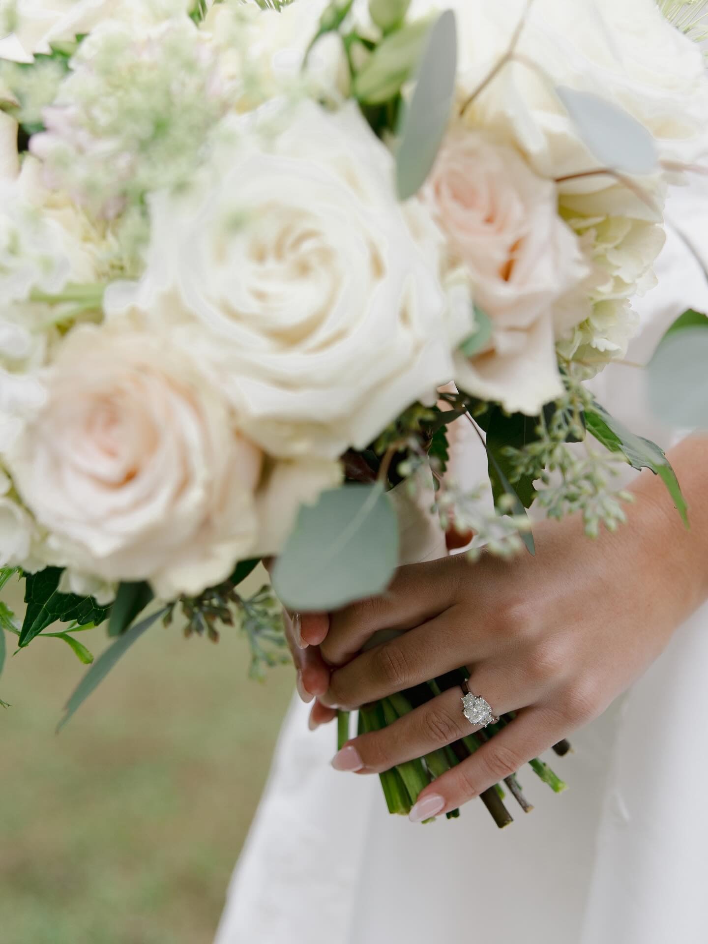 Bride holding white rose bouquet displaying diamond engagement ring