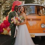 Bride holding bouquet stands next to orange vintage Volkswagen van photo booth