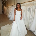 Bride trying on strapless ballgown wedding dress with textured fabric and dramatic train in bridal salon