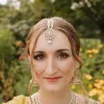 Bride in yellow and gold embroidered South Asian wedding attire with pearl tikka and statement jewelry in garden setting