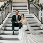 Newlyweds on decorated staircase with cascading white florals, candles, and bride's flowing veil
