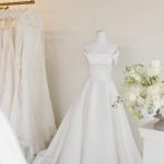 White wedding dresses displayed on mannequins in bridal boutique with floral arrangement