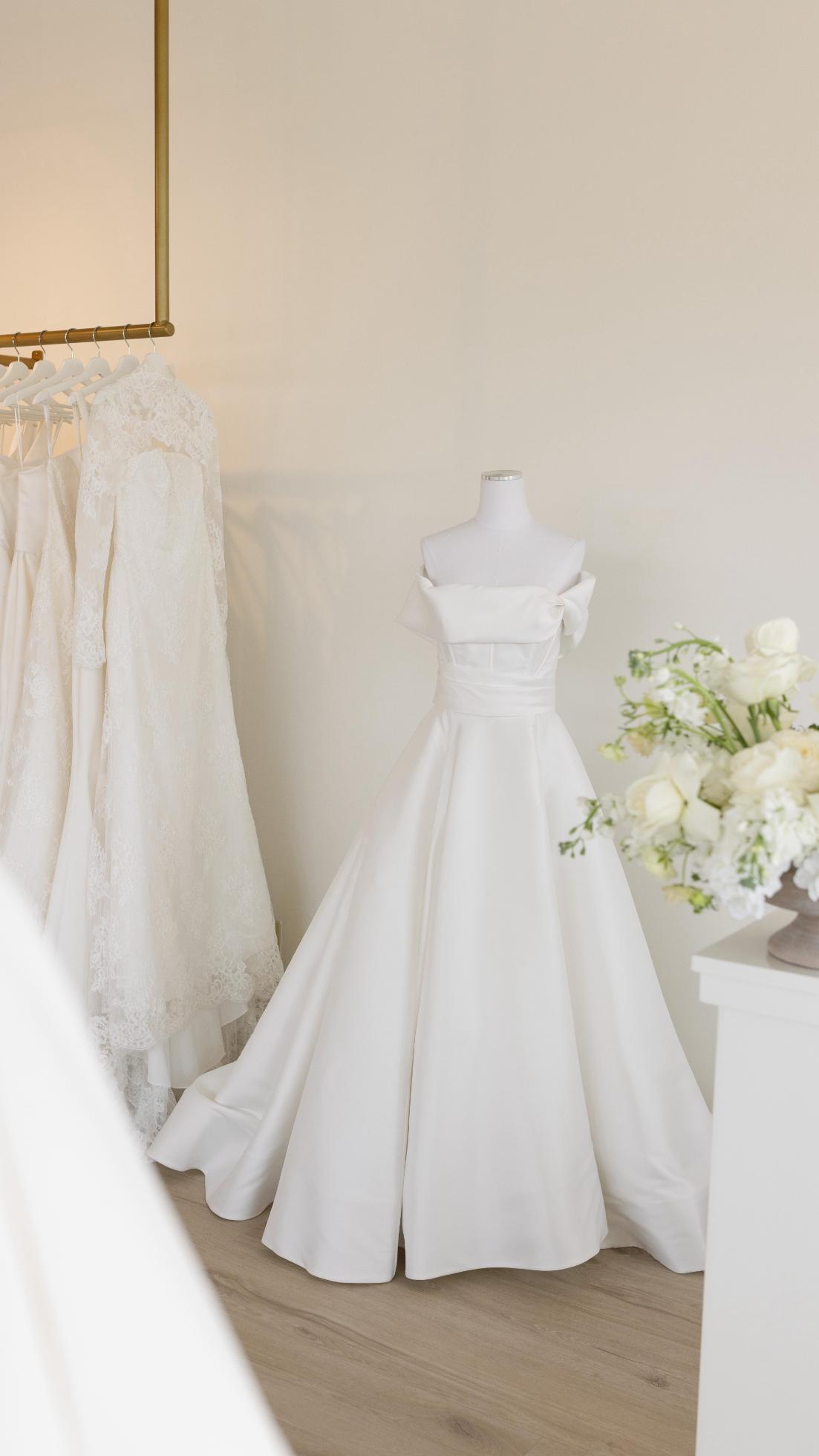 White wedding dresses displayed on mannequins in bridal boutique with floral arrangement