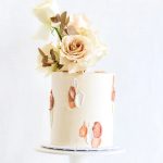 Modern single-tier wedding cake with abstract brushstroke design in rose gold and cream, topped with champagne-colored roses