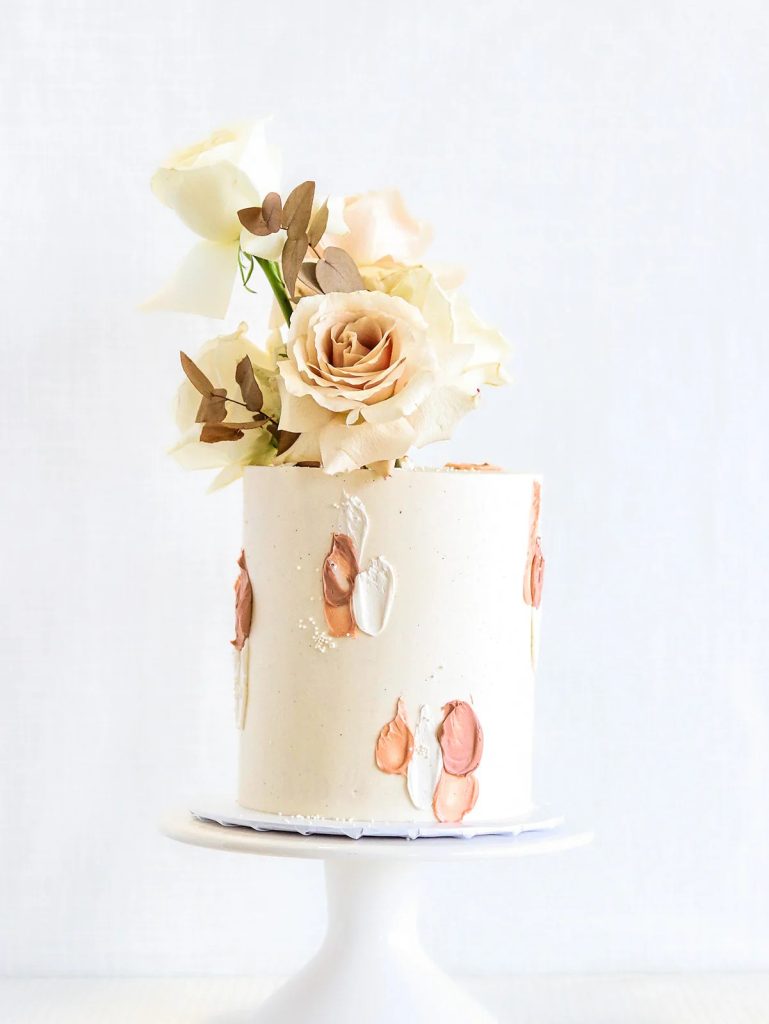 Modern single-tier wedding cake with abstract brushstroke design in rose gold and cream, topped with champagne-colored roses