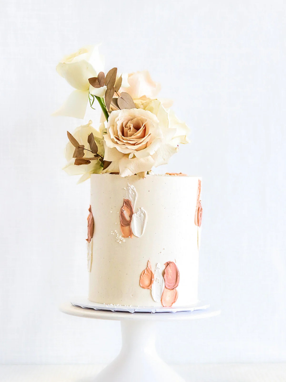 Modern single-tier wedding cake with abstract brushstroke design in rose gold and cream, topped with champagne-colored roses