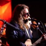 Male vocalist with beard and sunglasses singing and playing acoustic guitar during wedding performance