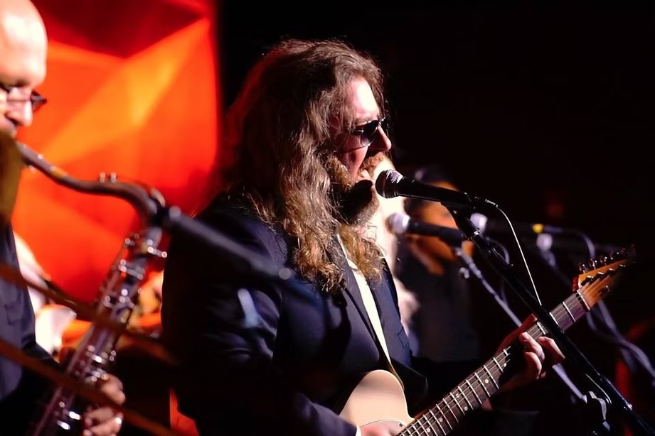Male vocalist with beard and sunglasses singing and playing acoustic guitar during wedding performance