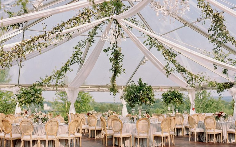Outdoor tented reception with greenery garlands, chandeliers, and round-back chairs overlooking mountain views