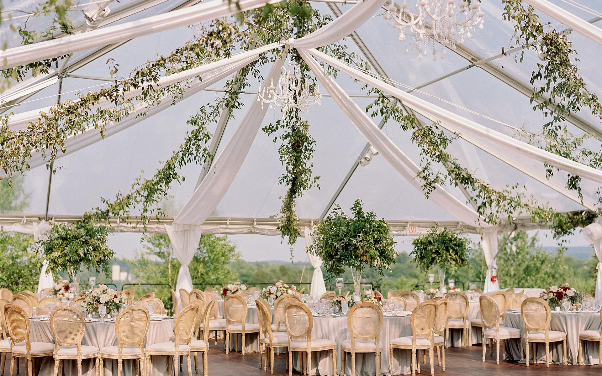 Outdoor tented reception with greenery garlands, chandeliers, and round-back chairs overlooking mountain views