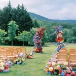 Wide view of outdoor mountain wedding ceremony with colorful floral arch and aisle decorations on green lawn