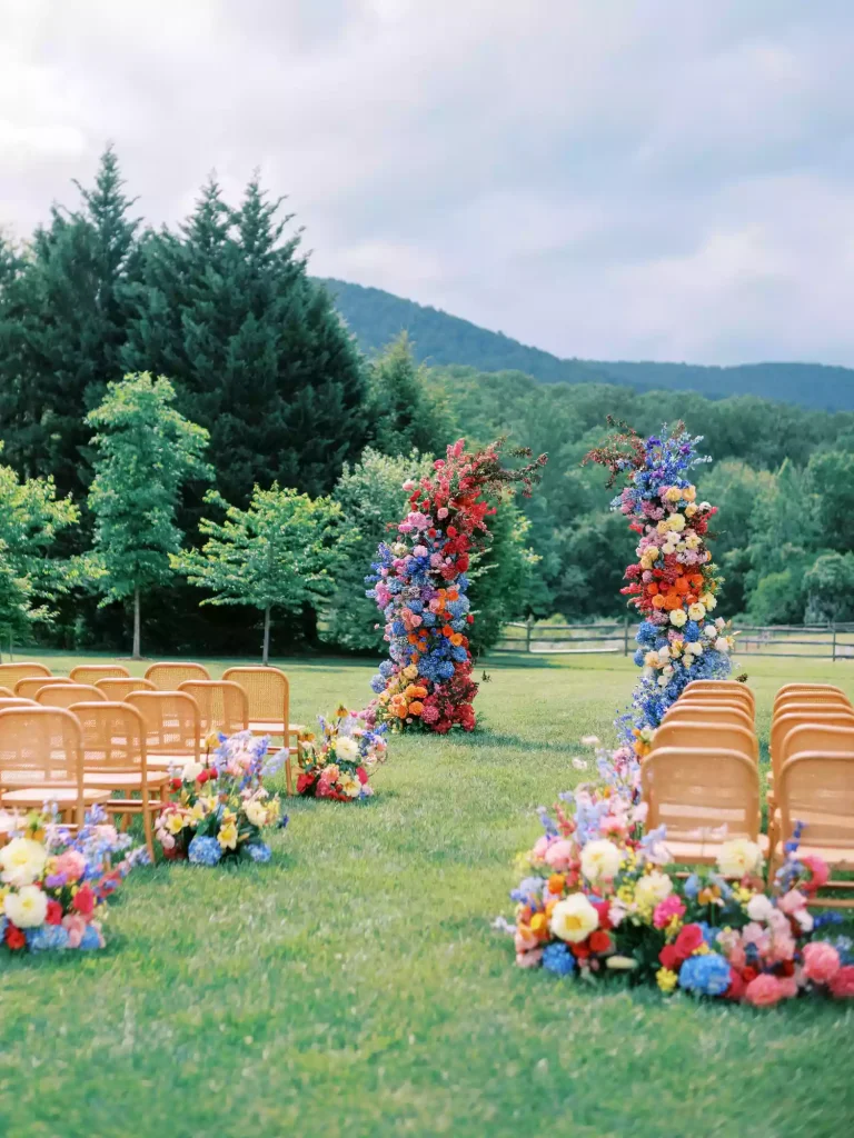Wide view of outdoor mountain wedding ceremony with colorful floral arch and aisle decorations on green lawn
