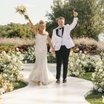 Newlyweds celebrating on outdoor ceremony aisle with white floral arrangements