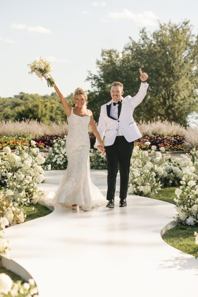 Newlyweds celebrating on outdoor ceremony aisle with white floral arrangements