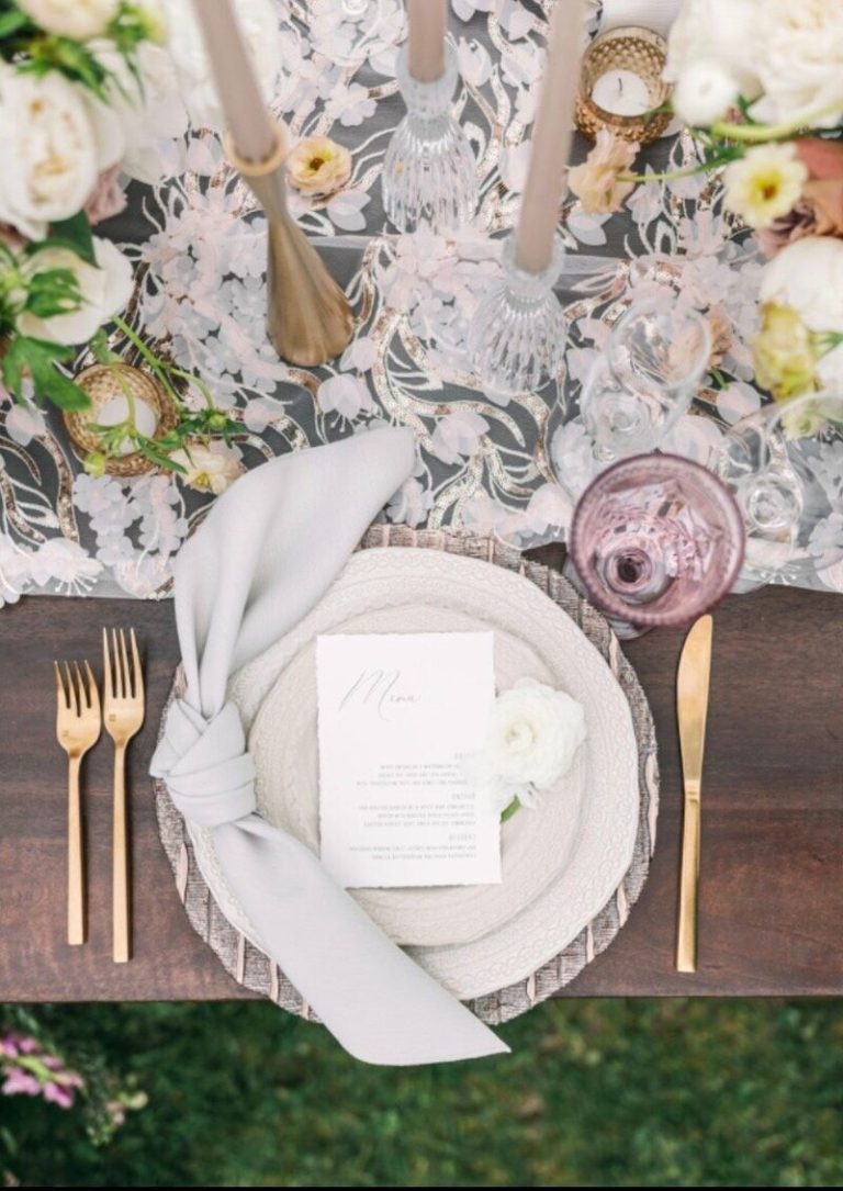 Overhead view of wedding place setting with menu card, pale blue napkin, gold flatware, and floral-patterned table runner