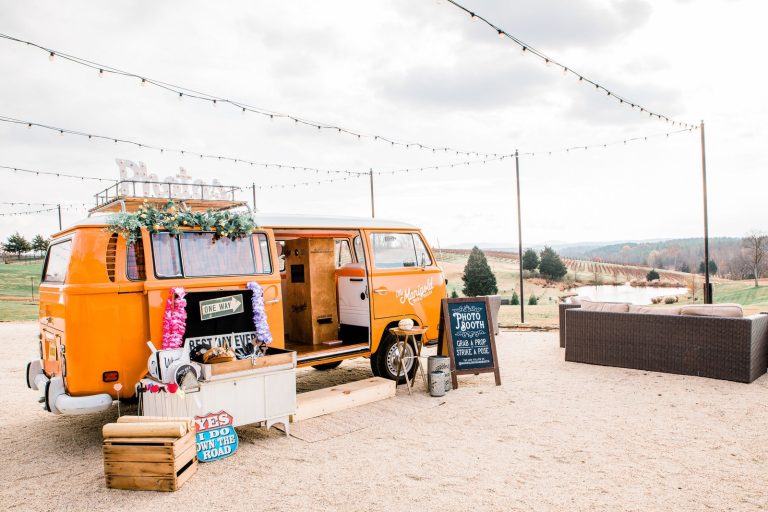 Orange retro Volkswagen photo booth van with wooden crates and props at wedding reception venue