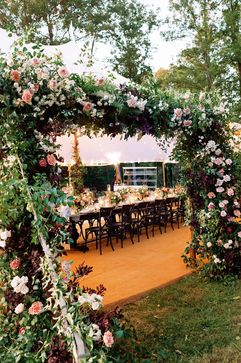 Outdoor wedding ceremony setup with floral arch and rows of chairs under trees