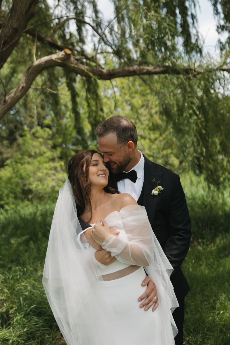 Groom carrying bride beneath weeping willow trees in romantic outdoor setting