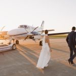 Bride and groom walking toward private airplane on tarmac at golden hour