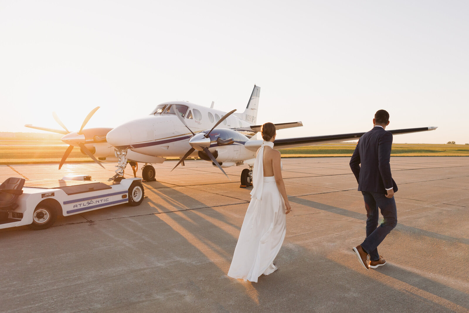 Bride and groom walking toward private airplane on tarmac at golden hour