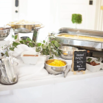 Catered buffet table with chafing dishes, mashed potato bar toppings, and eucalyptus greenery garland