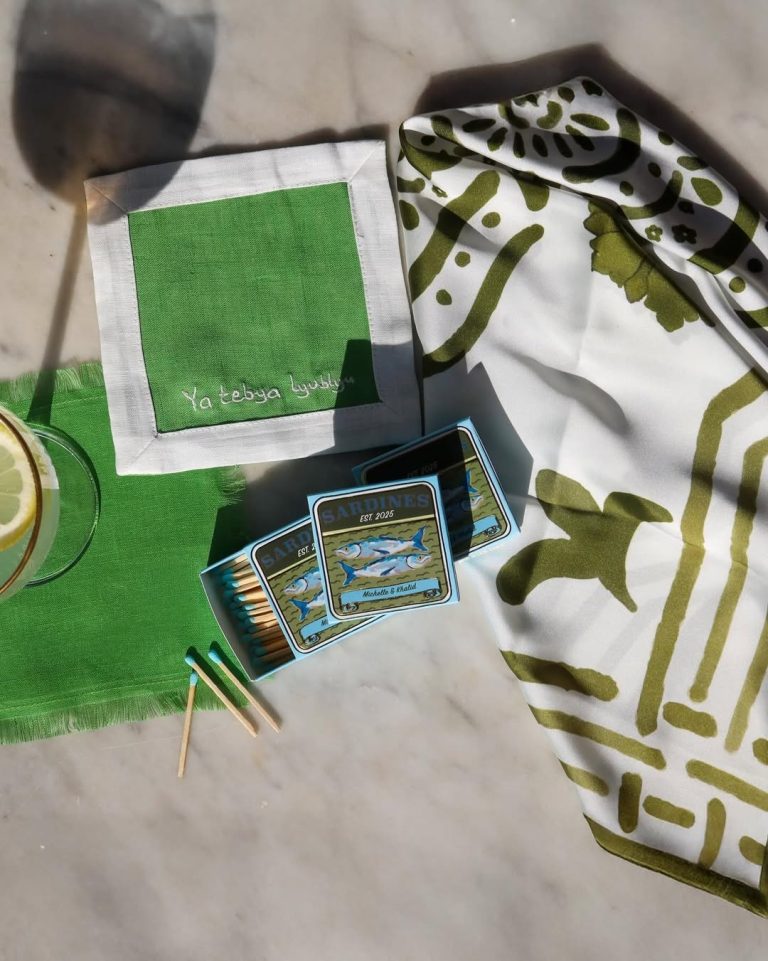Green matchbooks and vintage-style favor tags displayed on white cloth with gold accessories