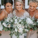 Bride and bridesmaids in champagne dresses holding white and eucalyptus bouquets showcasing coordinated wedding beauty looks