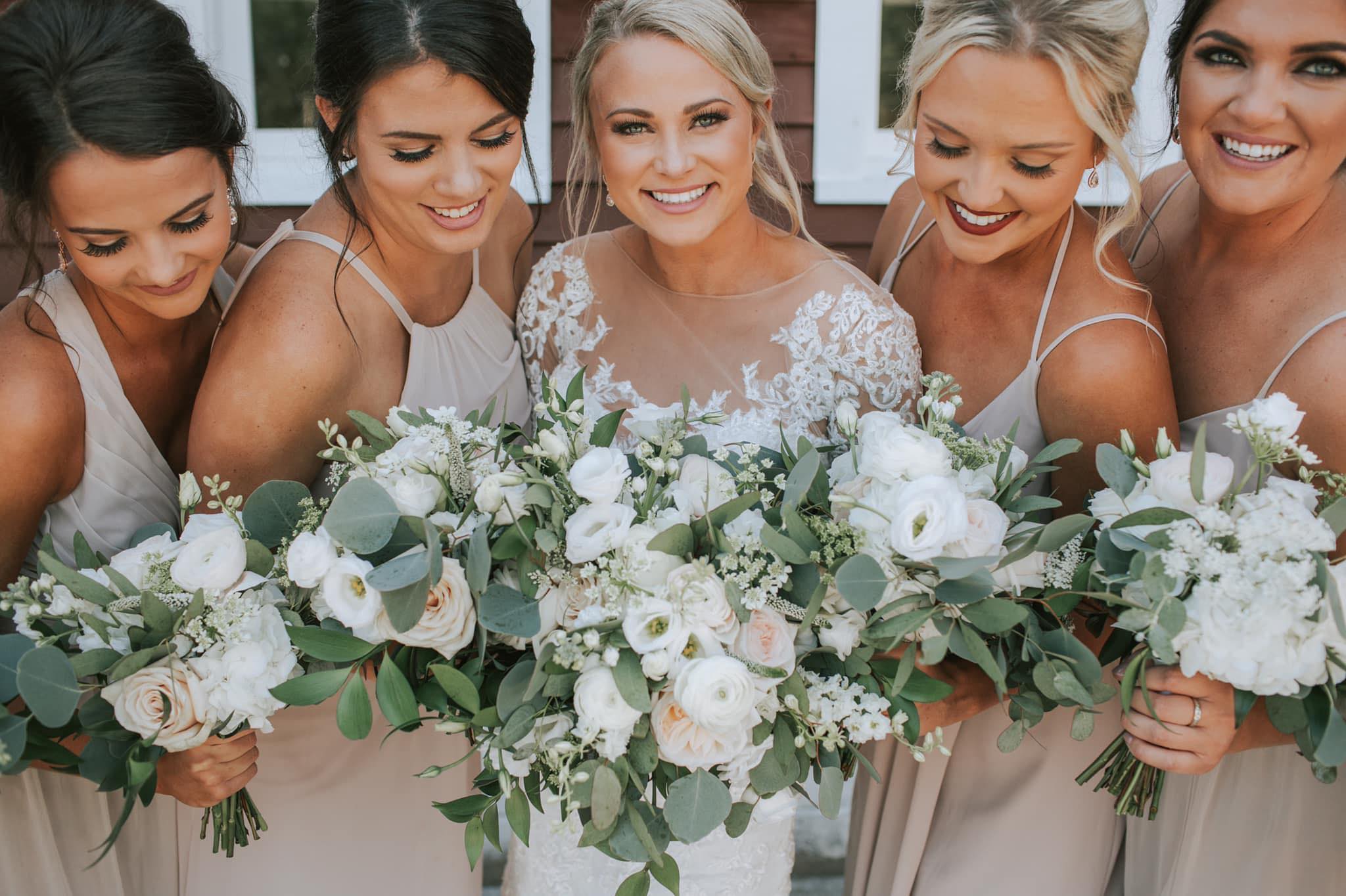 Bride and bridesmaids in champagne dresses holding white and eucalyptus bouquets showcasing coordinated wedding beauty looks