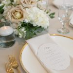 Wedding place setting detail with gold-rimmed china, menu card, and romantic centerpiece