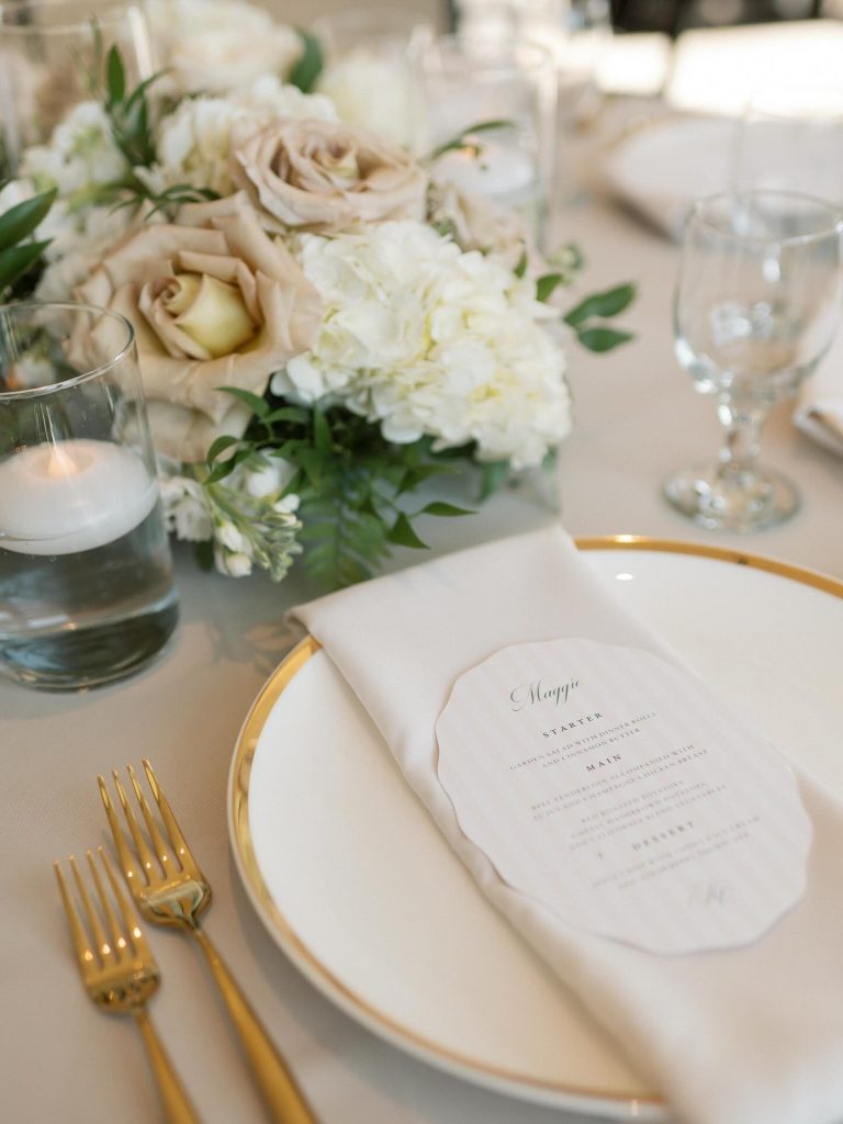 Wedding place setting detail with gold-rimmed china, menu card, and romantic centerpiece