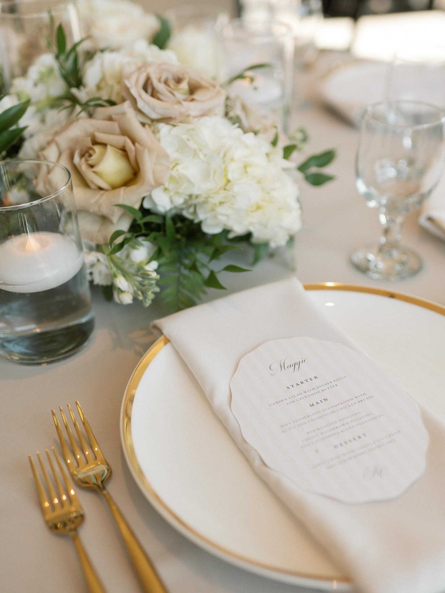 Wedding place setting detail with gold-rimmed china, menu card, and romantic centerpiece