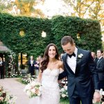 Newlyweds walking down aisle after ceremony in garden venue with floral-lined pathway and ivy-covered hedge backdrop