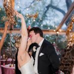 Bride and groom dancing together under string lights at evening wedding reception