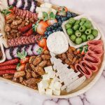 Wooden charcuterie board with assorted meats, cheeses, olives, nuts, and fresh fruits for wedding catering