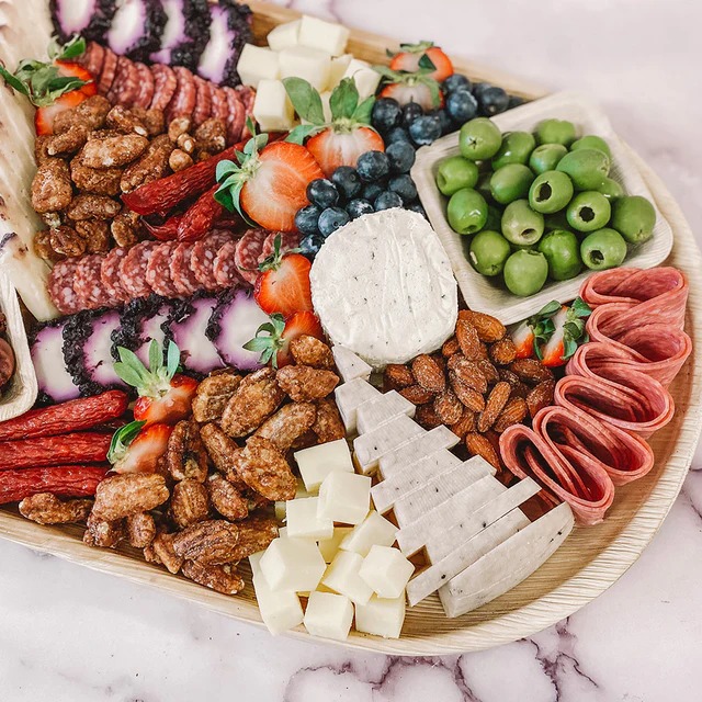 Wooden charcuterie board with assorted meats, cheeses, olives, nuts, and fresh fruits for wedding catering