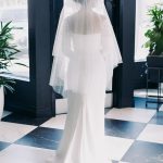 Bride from behind wearing tiered veil and sleek wedding gown with train on geometric tiled floor