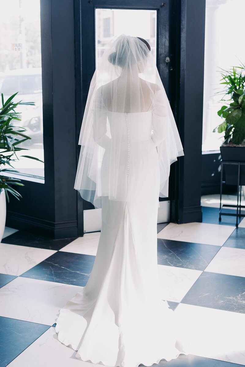 Bride from behind wearing tiered veil and sleek wedding gown with train on geometric tiled floor