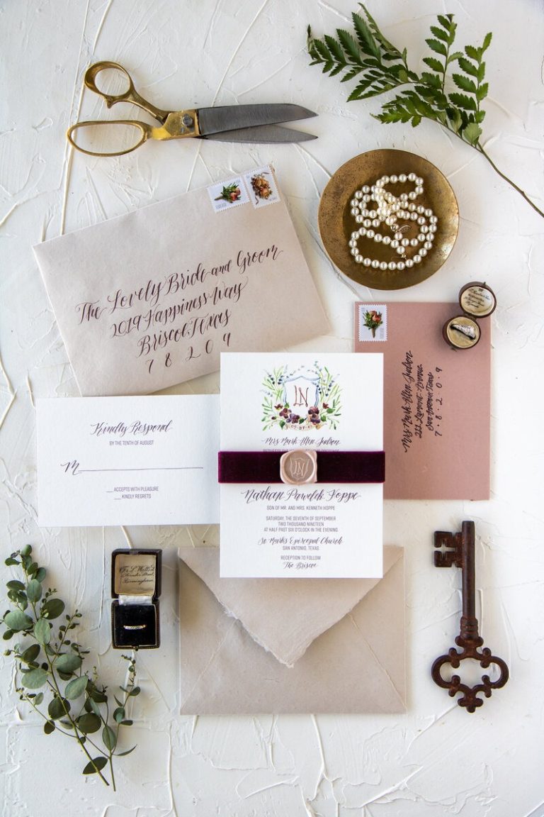 Wedding invitation suite flatlay featuring calligraphied envelopes, floral invitation with wax seal, vintage scissors, pearls, and botanical elements