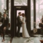 Bride and groom silhouetted in Hotel Deco's grand entrance with floral arch and natural window light