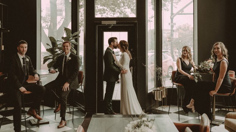 Bride and groom silhouetted in Hotel Deco's grand entrance with floral arch and natural window light